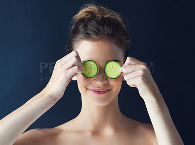Buy stock photo Cropped shot of a beautiful young woman holding cucumbers over her eyes