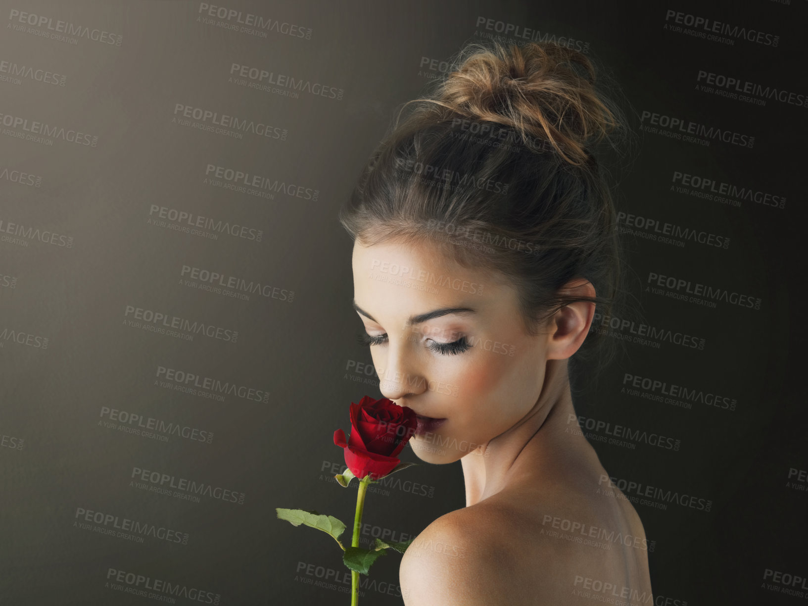 Buy stock photo Shot of a young woman holding a red rose against a dark background