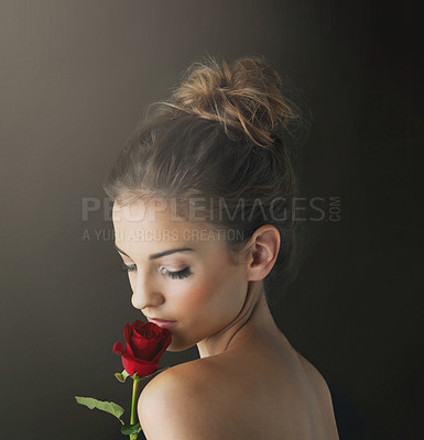 Buy stock photo Shot of a young woman holding a red rose against a dark background