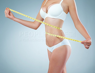 Buy stock photo Shot of an unidentifiable young woman using a measuring tape to measure her waist in studio