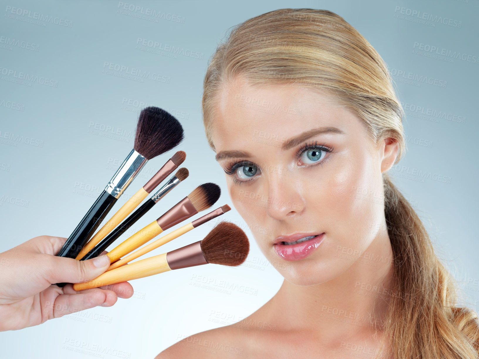 Buy stock photo Studio portrait of a beautiful young woman posing with makeup brushes against a blue background