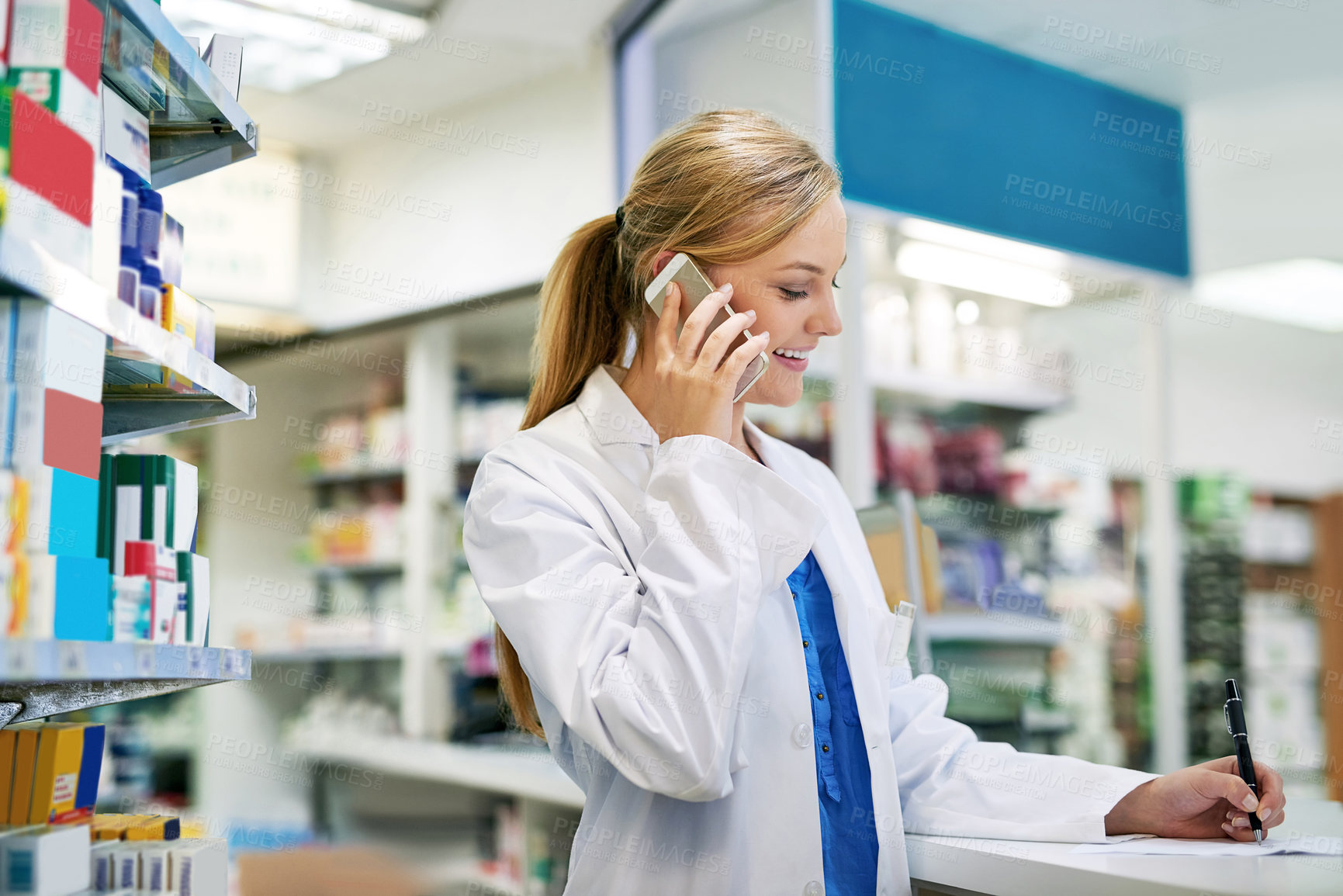 Buy stock photo Shot of a young pharmacist talking on a cellphone while filling out a prescription in a chemist