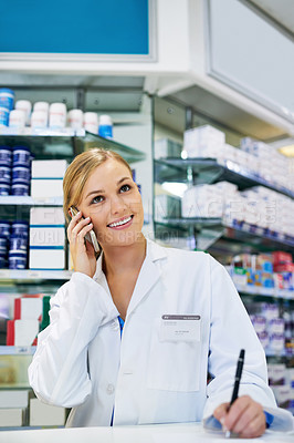 Buy stock photo Shot of a young pharmacist talking on a cellphone while filling out a prescription in a chemist
