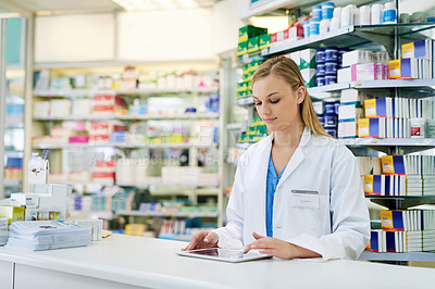 Buy stock photo Shot of a young pharmacist using a digital tablet at the checkout counter