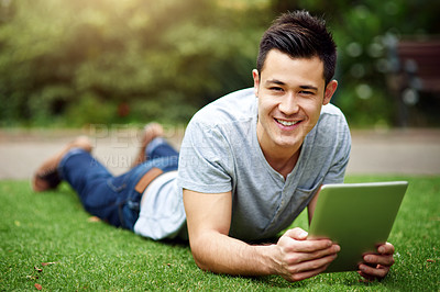 Buy stock photo Portrait of a handsome young man using a digital tablet while lying on the grass outside