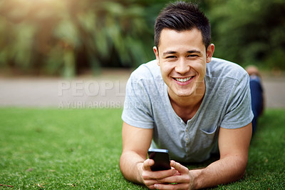 Buy stock photo Portrait of a handsome young man using a cellphone while lying on the grass outside