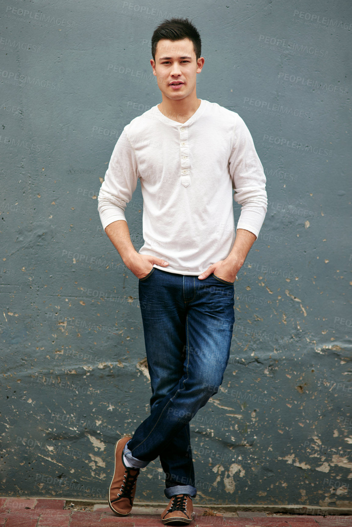 Buy stock photo Portrait of a handsome young man standing with his hands in his pockets against a grey wall