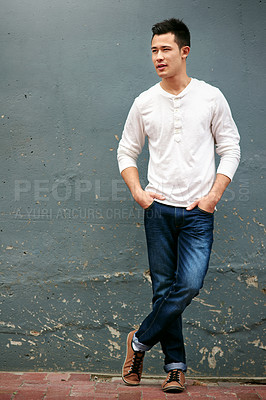 Buy stock photo Shot of a handsome young man standing with his hands in his pockets against a grey wall