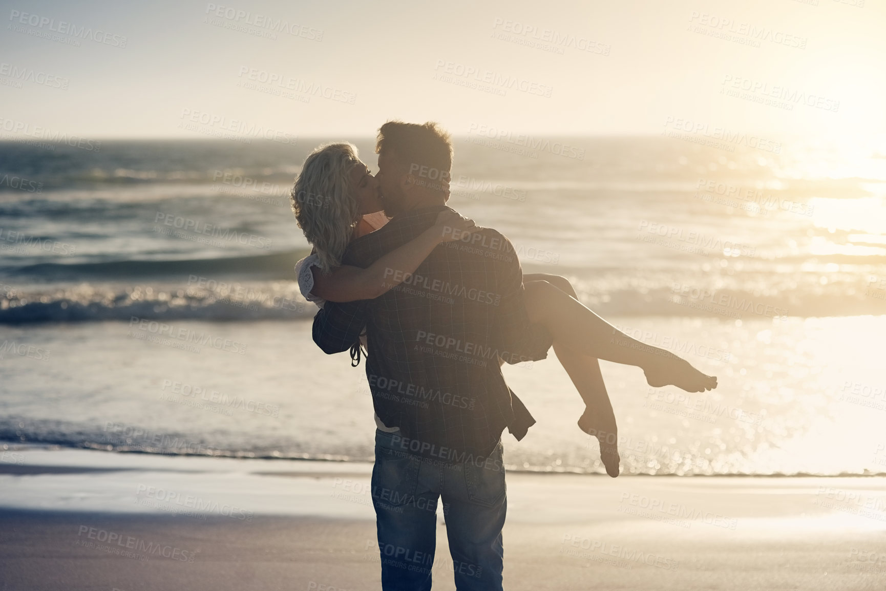 Buy stock photo Shot of a loving couple sharing a kiss while spending time at the beach