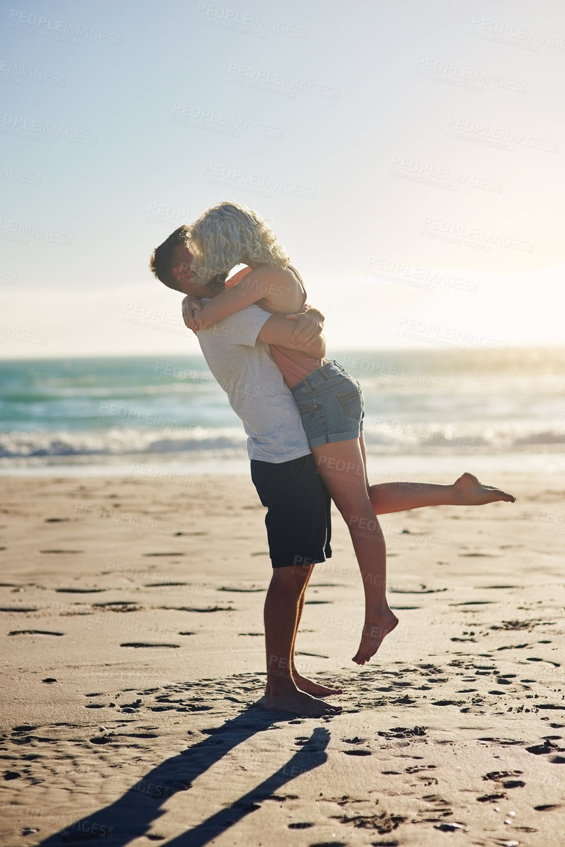 Buy stock photo Shot of a loving couple sharing a kiss while spending time at the beach