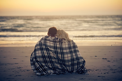 Buy stock photo Rearview shot of a young couple sitting on the beach with a blanket wrapped around them