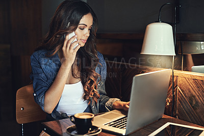 Buy stock photo Shot of a young woman answering her cellphone while using her laptop in a coffee shop