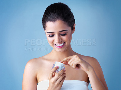Buy stock photo Studio shot of a beautiful young woman applying face cream against a blue background