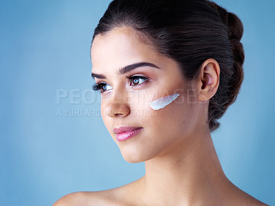 Buy stock photo Studio shot of a beautiful young woman posing with lotion on her face against a blue background