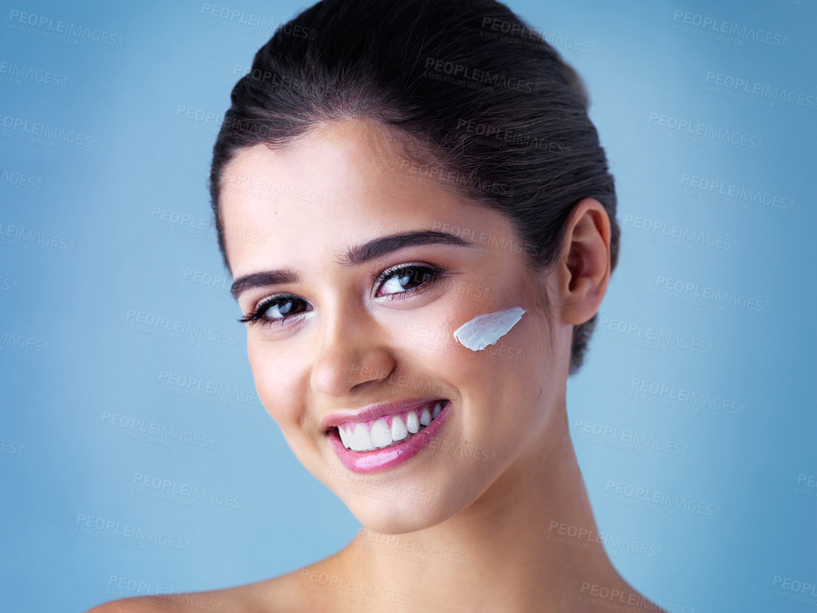 Buy stock photo Studio portrait of a beautiful young woman posing with lotion on her face against a blue background