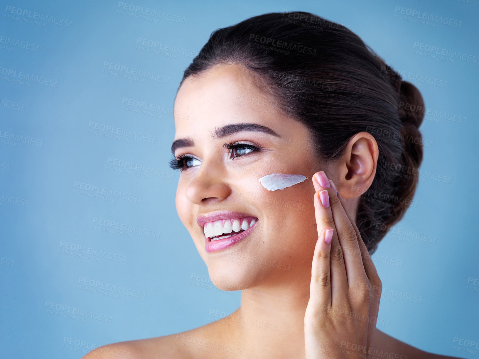 Buy stock photo Happy woman, beauty and skincare with cream for facial treatment on a blue studio background. Female person or young model applying cosmetics or anti aging lotion for dermatology or cosmetology