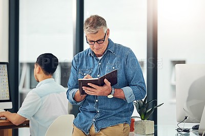Buy stock photo Shot of a creative entrepreneur making notes in his notebook while standing in the office