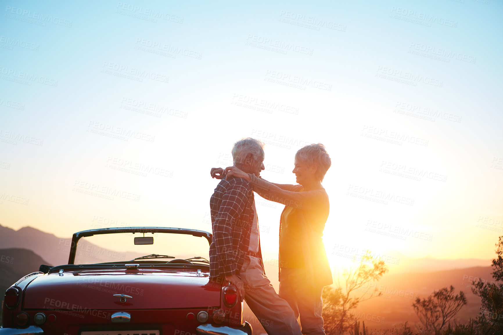 Buy stock photo Shot of an affectionate senior couple enjoying the sunset during a roadtrip