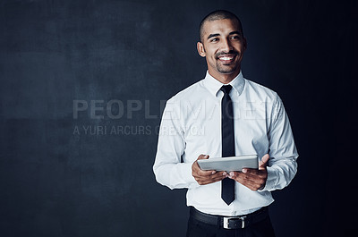 Buy stock photo Studio shot of a young businessman looking thoughtful while using a digital tablet against a dark background