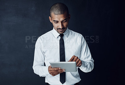 Buy stock photo Studio shot of a young businessman using a digital tablet against a dark background