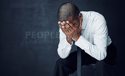 Buy stock photo Studio shot of a young businessman sitting with his hands covering his face against a dark background