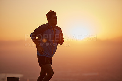 Buy stock photo Shot of a silhouetted young man out for a run at sunrise