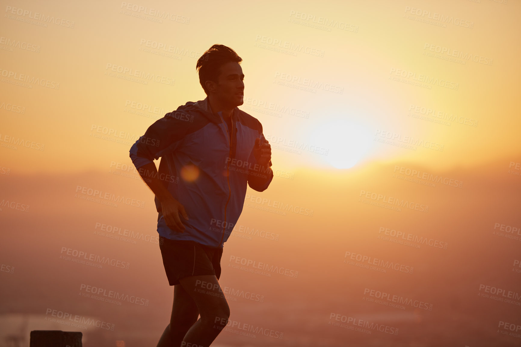 Buy stock photo Shot of a silhouetted young man out for a run at sunrise