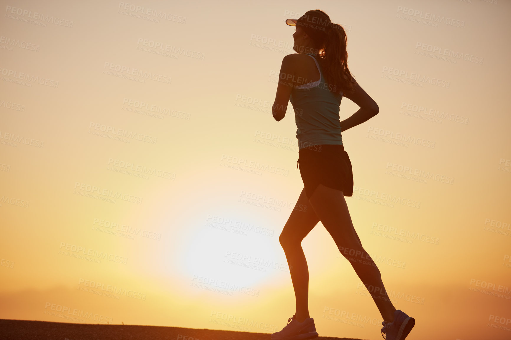 Buy stock photo Shot of a silhouetted young woman out for a run at sunrise