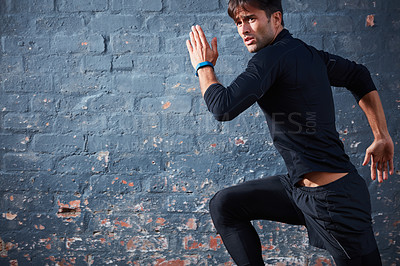 Buy stock photo Shot of a focussed young man working out next to a brick wall outside