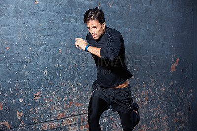 Buy stock photo Shot of a focussed young man working out next to a brick wall outside