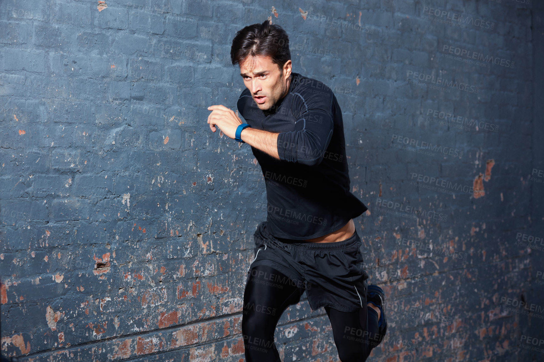 Buy stock photo Shot of a focussed young man working out next to a brick wall outside