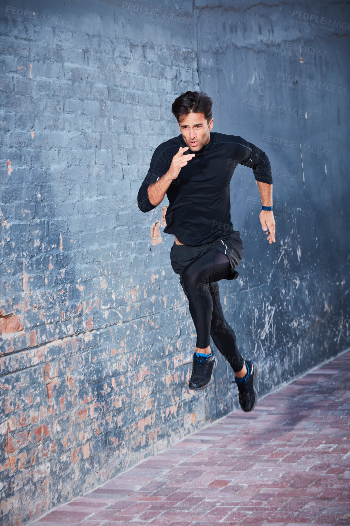 Buy stock photo Shot of a focussed young man working out next to a brick wall outside