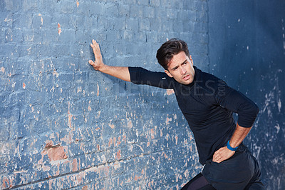 Buy stock photo Shot of a focussed young man working out next to a brick wall outside