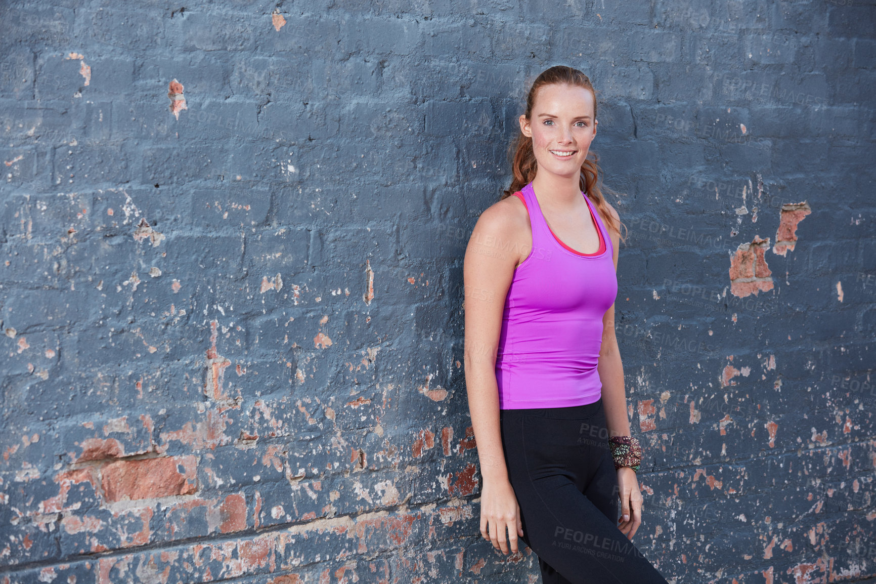 Buy stock photo Portrait of a happy young woman working out next to a brick wall outside