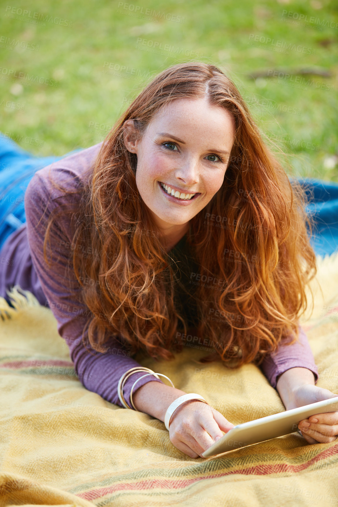 Buy stock photo Shot of a young woman using her tablet while relaxing at the park