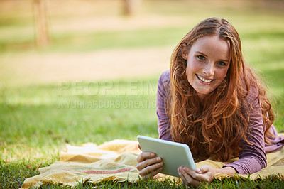 Buy stock photo Shot of a young woman using her tablet while relaxing at the park