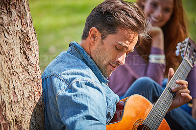 Buy stock photo Shot of a young man playing guitar to his girlfriend