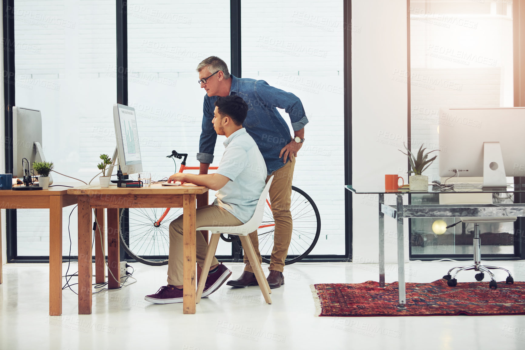 Buy stock photo Shot of a mature designer helping a younger colleague with some designs