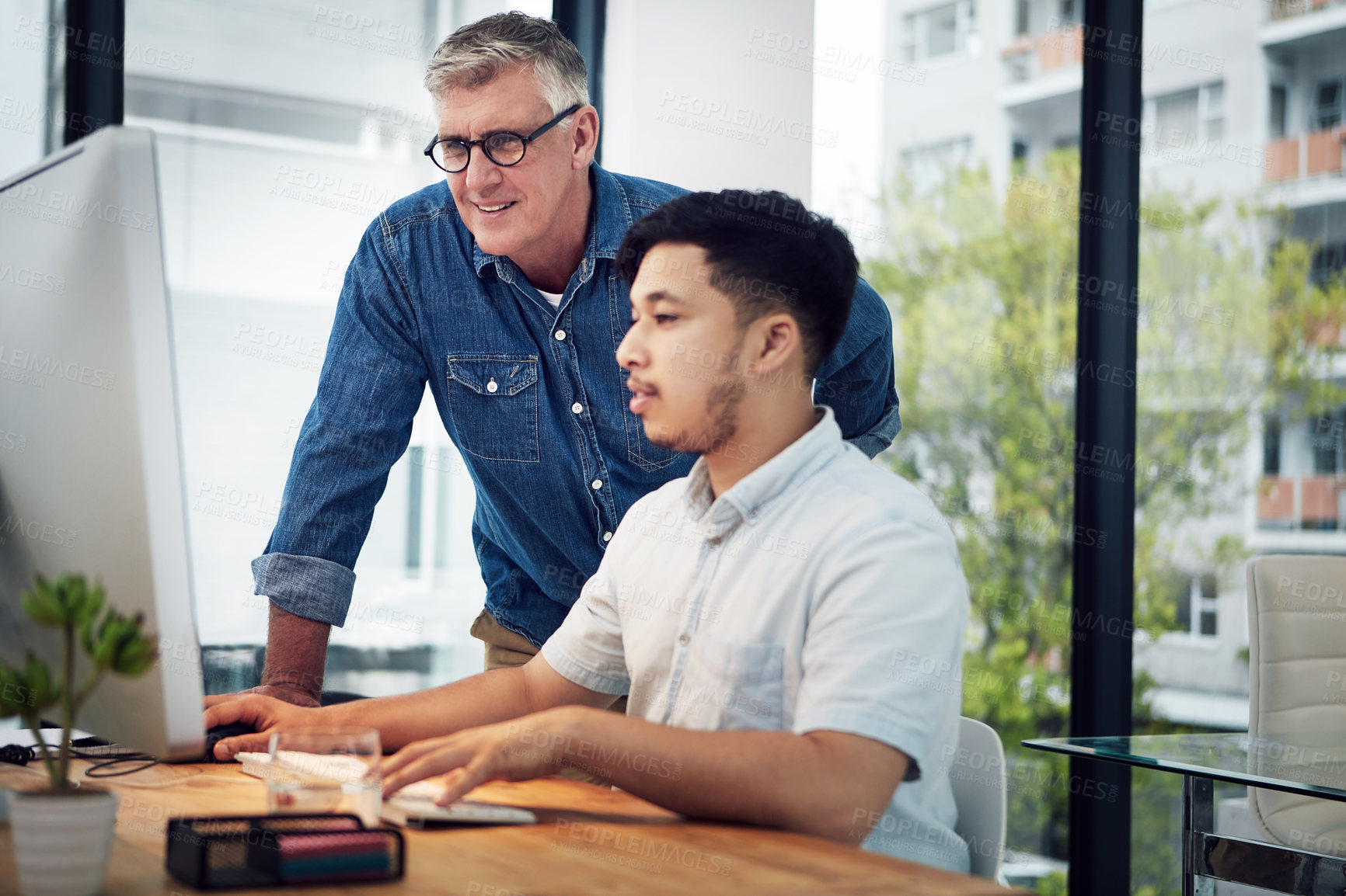 Buy stock photo Shot of a mature designer helping a younger colleague with some designs