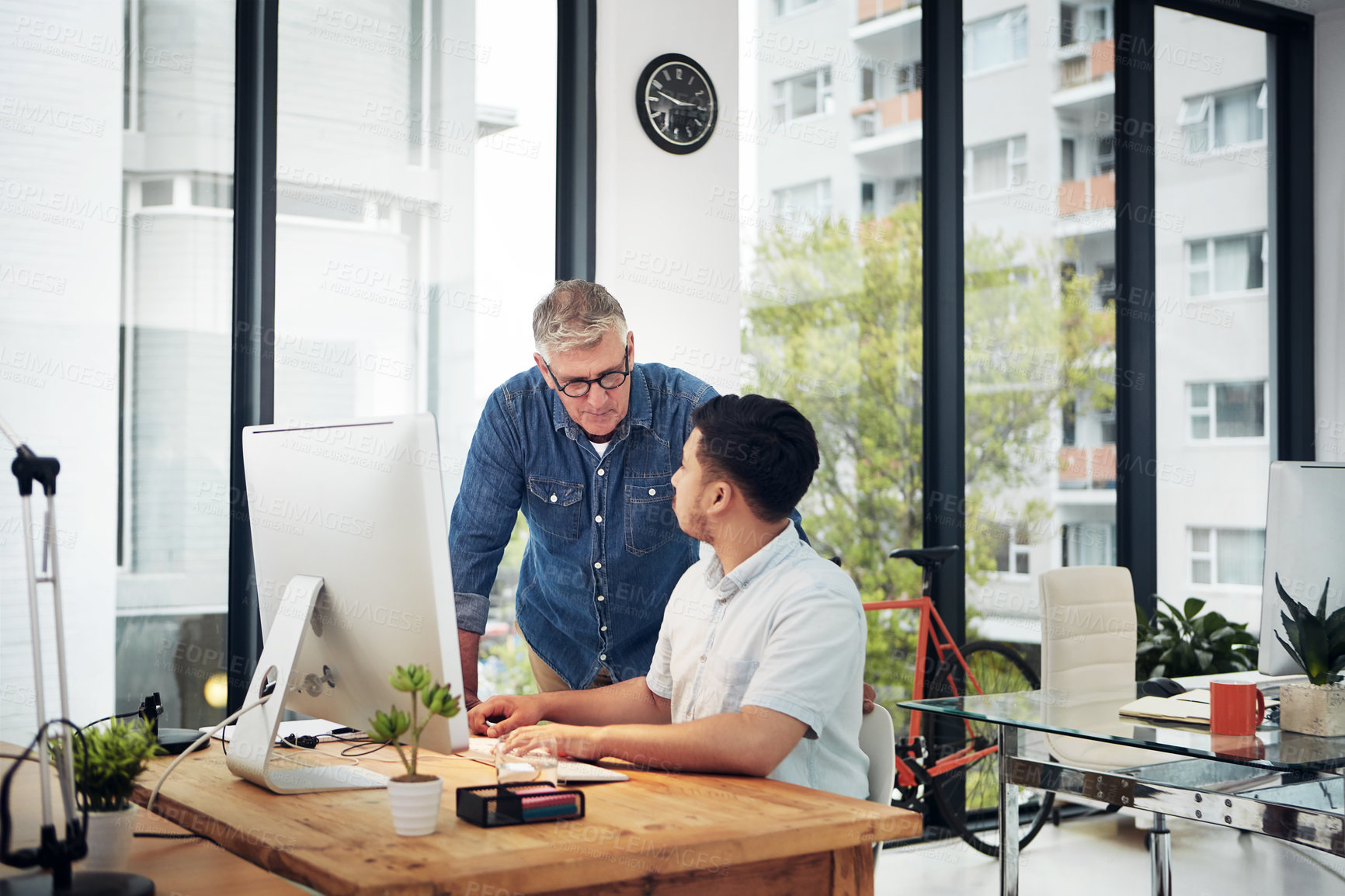 Buy stock photo Shot of a mature designer helping a younger colleague with some designs