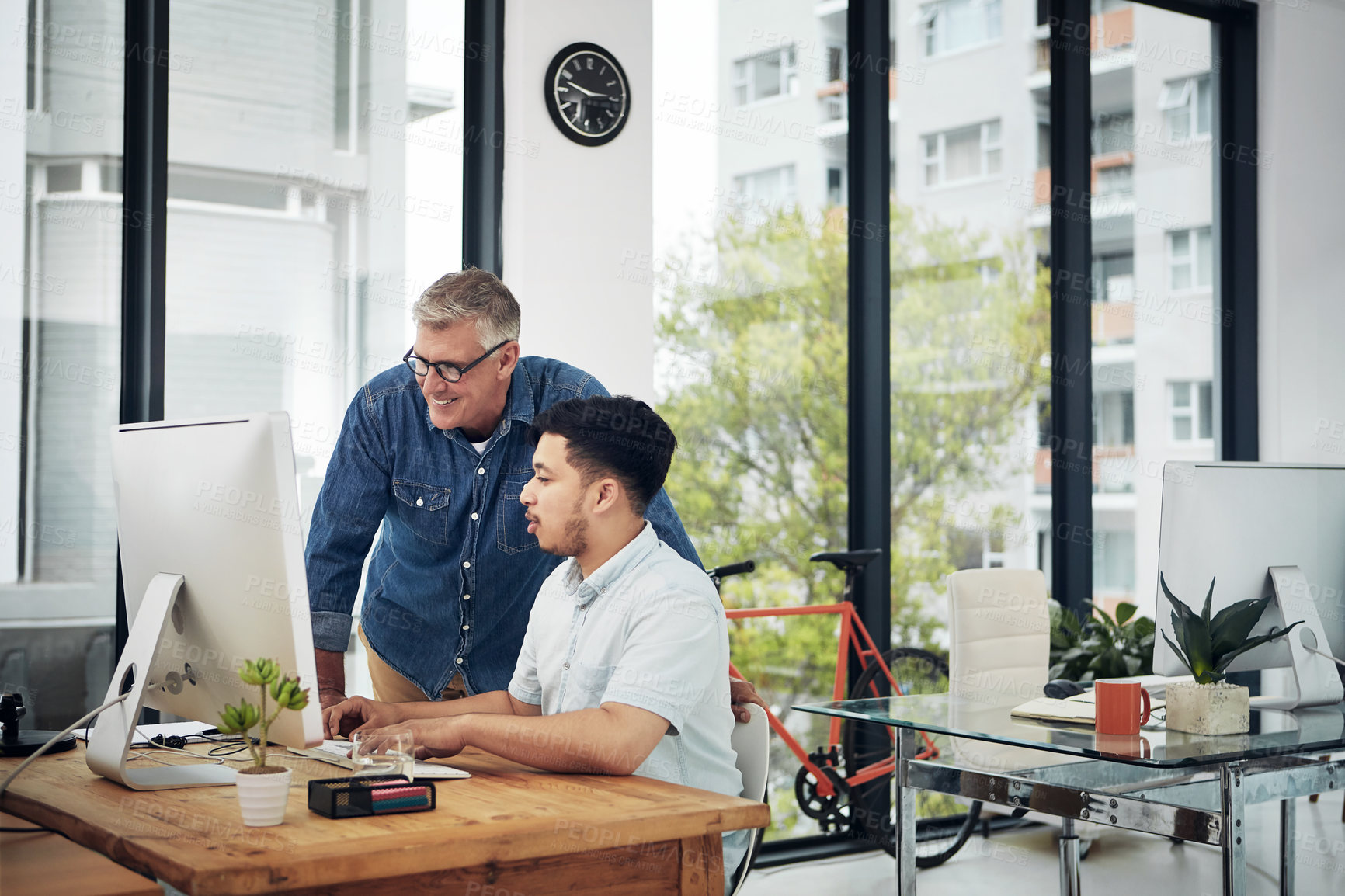 Buy stock photo Shot of a mature designer helping a younger colleague with some designs