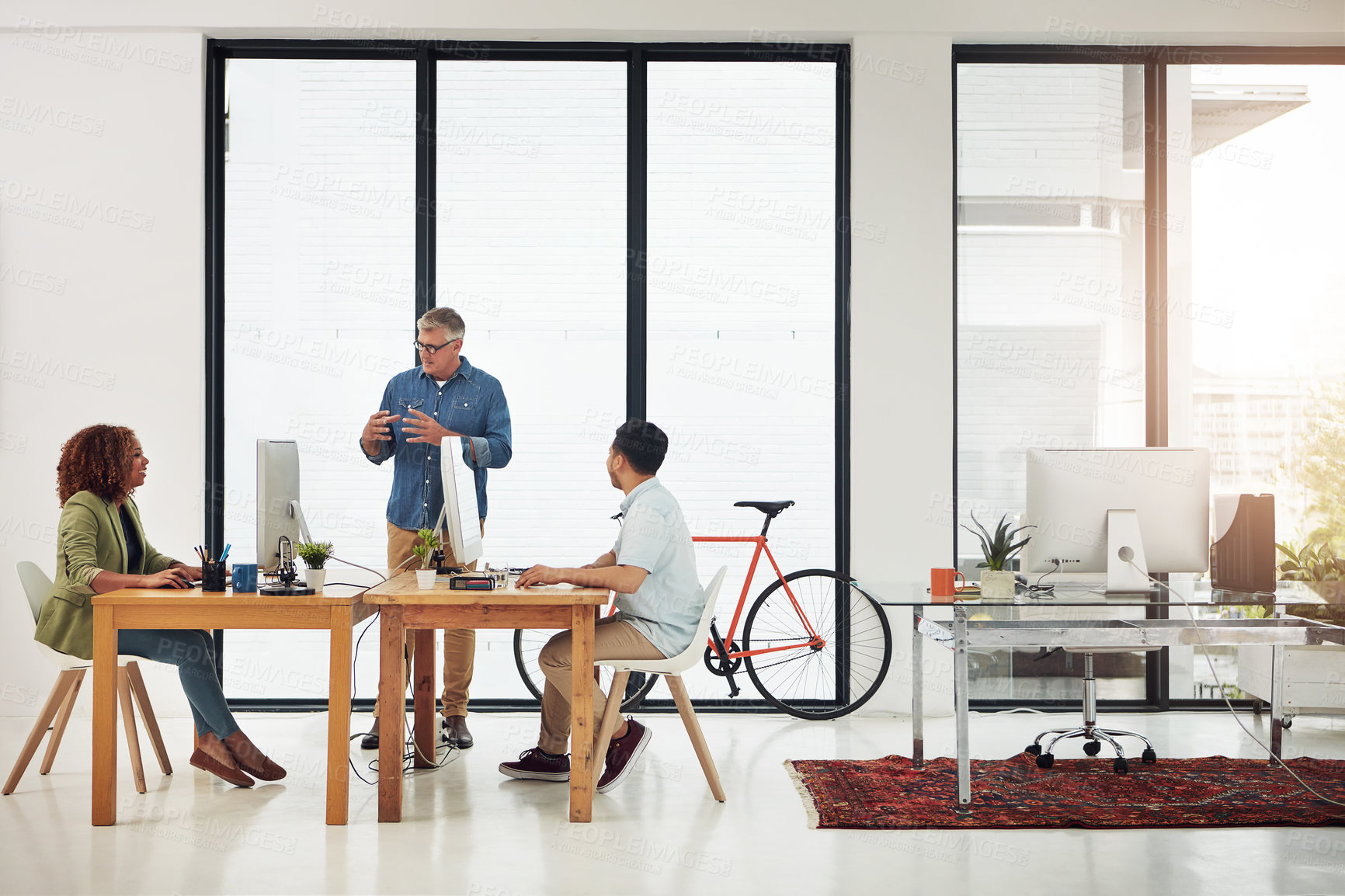 Buy stock photo Shot of a mature businessman addressing two employees in the office