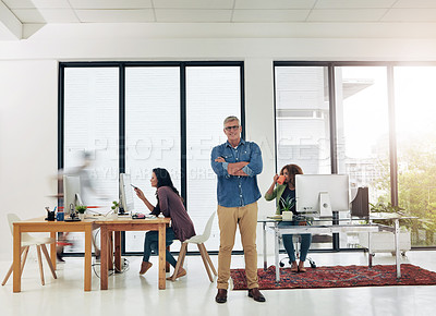 Buy stock photo Portrait of a mature designer standing in the office with his colleagues in the background