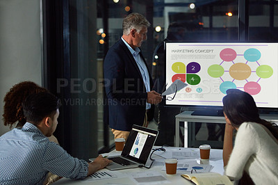 Buy stock photo Shot of a dedicated businessman giving a presentation to his colleagues in the boardroom after hours