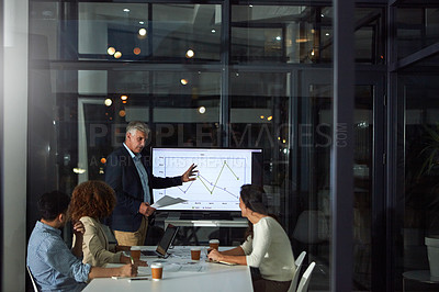 Buy stock photo Shot of a dedicated businessman giving a presentation to his colleagues in the boardroom after hours