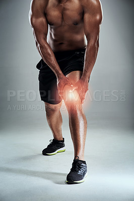 Buy stock photo Cropped shot of a sporty young man nursing a knee injury against a grey background