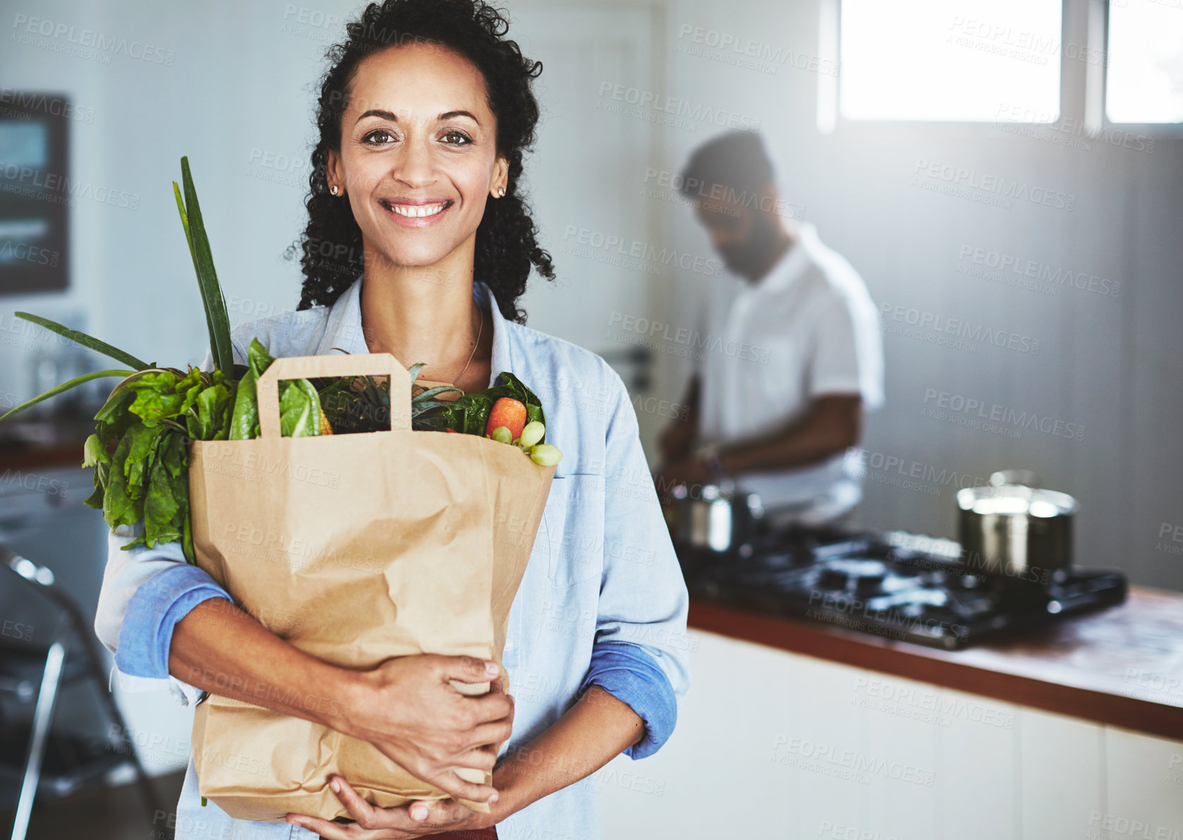 Buy stock photo Portrait of a happy woman holding a bag of fresh vegetables while standing in her kitchen