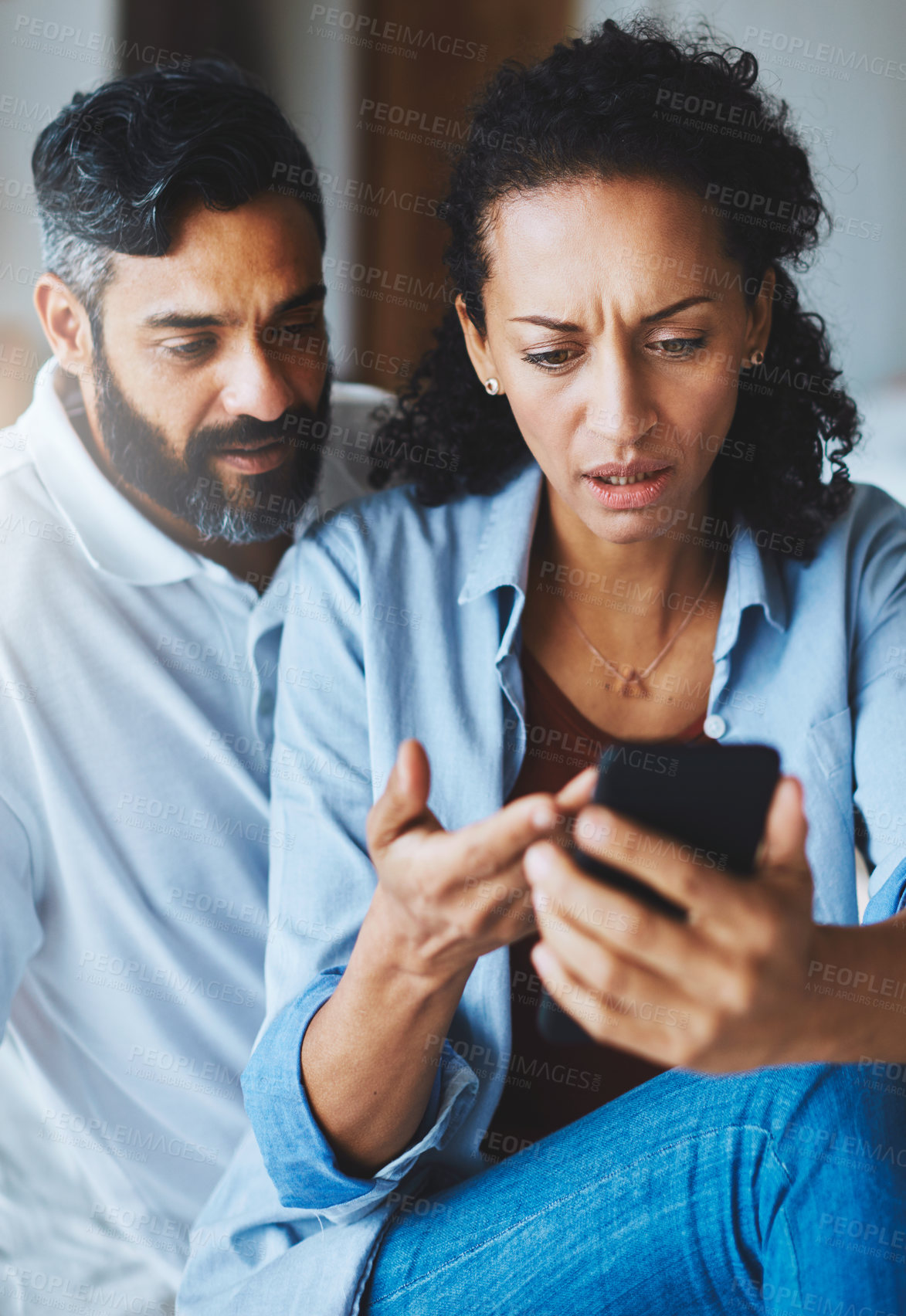 Buy stock photo Shot of a dismayed couple receiving bad news via a smartphone at home