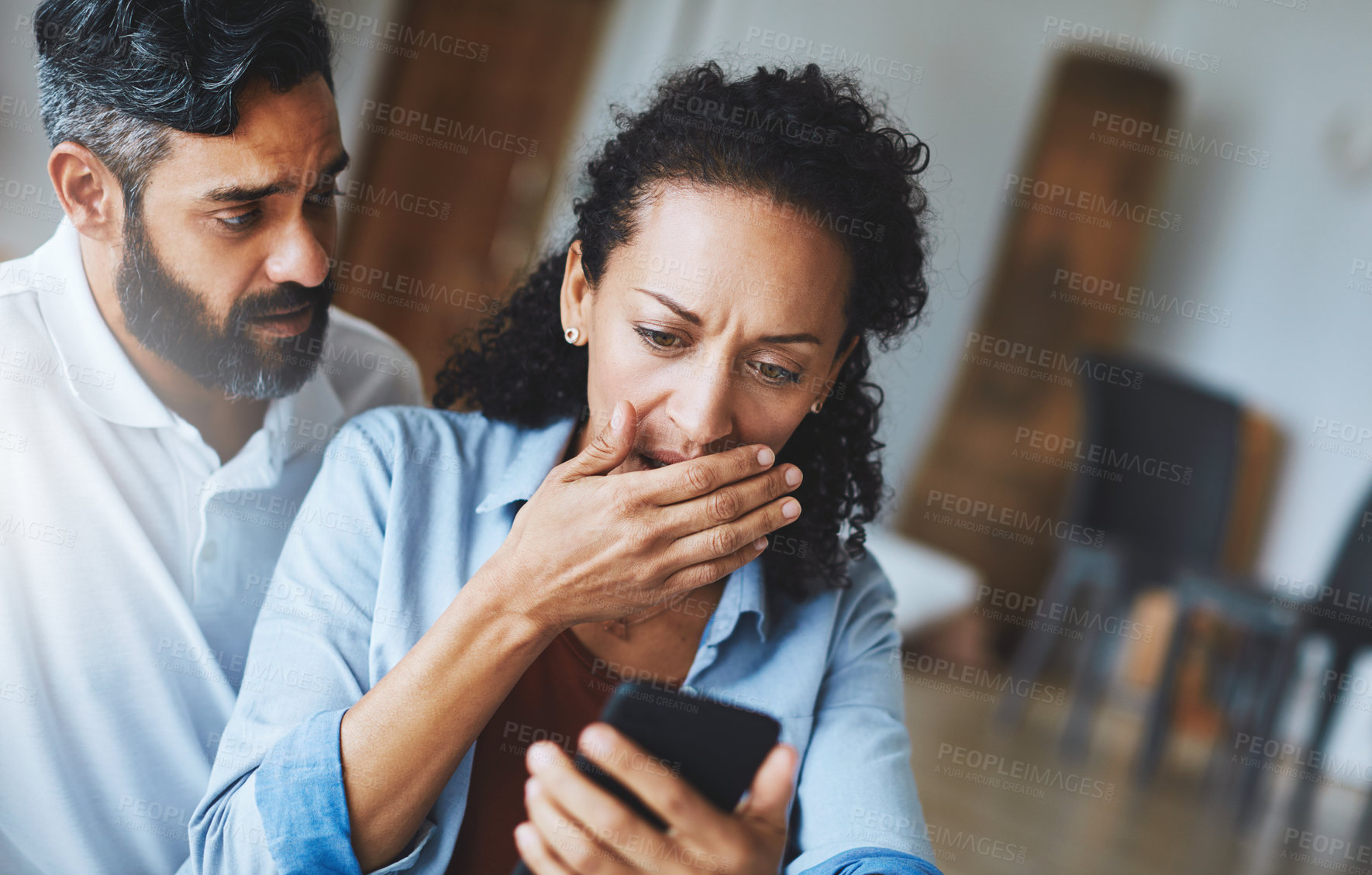 Buy stock photo Shot of a dismayed couple receiving bad news via a smartphone at home