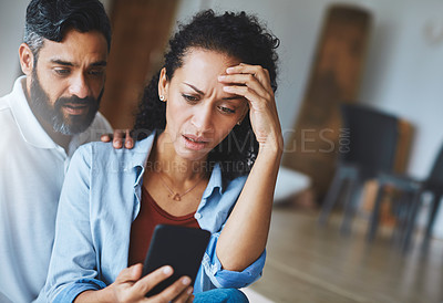 Buy stock photo Shot of a dismayed couple receiving bad news via a smartphone at home